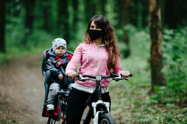 Menina com uma criança andando de bicicleta em uma máscara médica no rosto