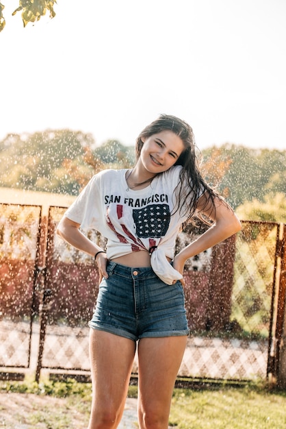 Menina com uma fonte no jardim ao pôr do sol. verão quente, camisa molhada. Bandeira dos EUA.