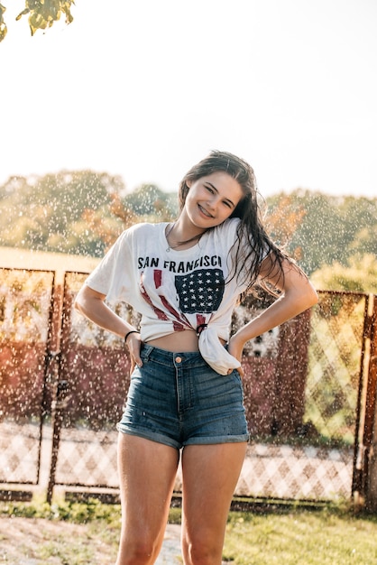 Foto menina com uma fonte no jardim ao pôr do sol. verão quente, camisa molhada. bandeira dos eua.