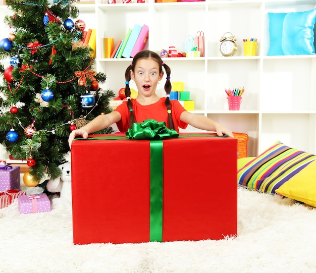 Menina com uma grande caixa de presente perto da árvore de Natal