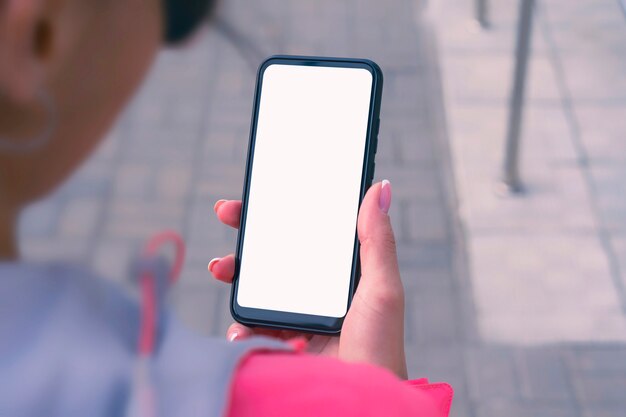 Menina com uma jaqueta rosa segura uma maquete de smartphone com tela branca nas mãos. Tecnologia mock-up.