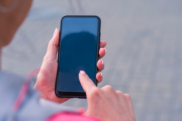 Menina com uma jaqueta rosa tem uma maquete de smartphone nas mãos. Tecnologia mock-up.