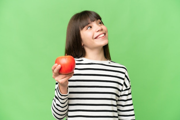 Menina com uma maçã sobre fundo croma chave isolado olhando para cima enquanto sorri