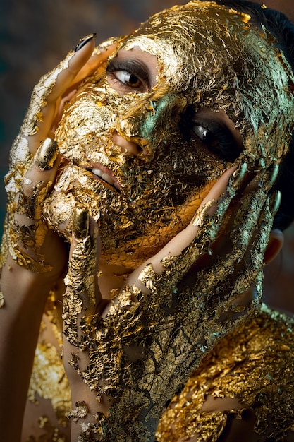 Menina com uma máscara feita de folha de ouro no rosto Retrato sombrio de uma morena no estúdio