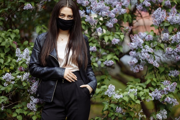 Menina com uma máscara médica em um fundo de lilases florescendo