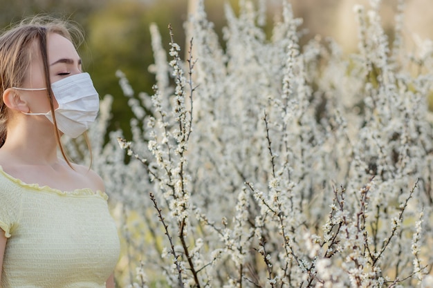 Menina com uma máscara médica. Menina na primavera entre o jardim florido.