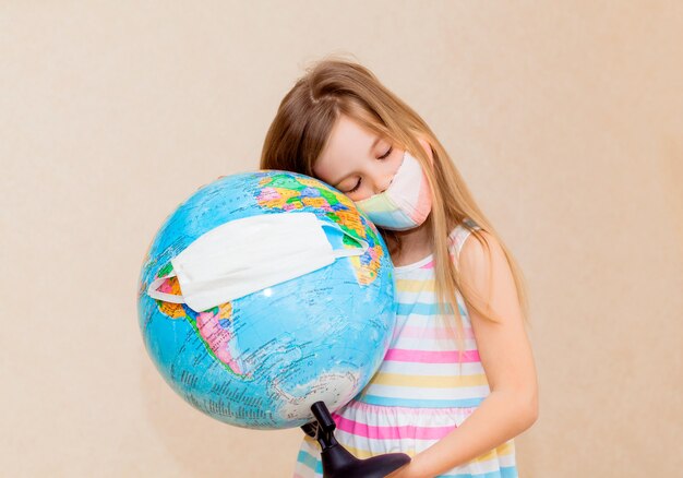 Menina com uma máscara médica tem um globo nas mãos, envolto em uma máscara médica.