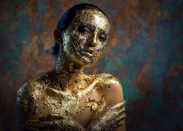 Menina com uma máscara no rosto feita de folha de ouro Retrato de estúdio sombrio de uma morena em um fundo abstrato