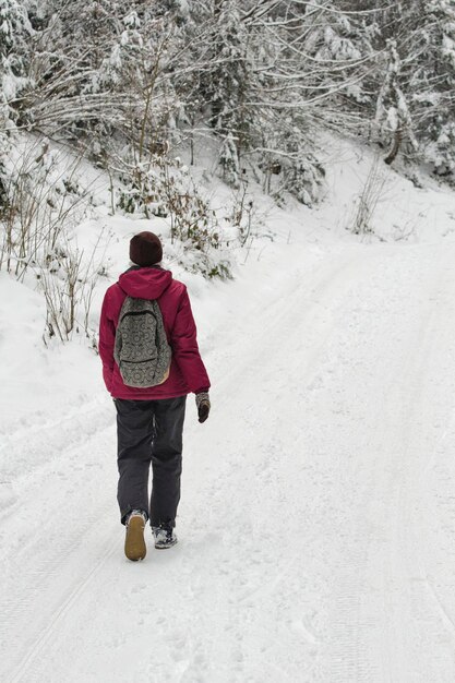 Menina com uma mochila andando pela estrada em uma floresta de neve Dia de inverno