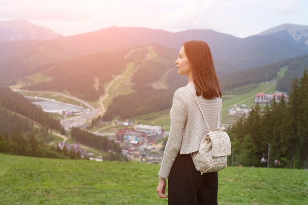 Menina com uma mochila de pé na colina e admirando as montanhas. Cidade à distância