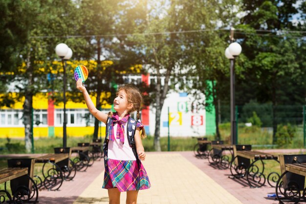 Menina com uma mochila e com um uniforme escolar no pátio da escola joga pop-lo brinquedo.