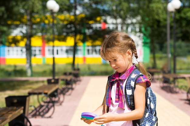 Menina com uma mochila e com um uniforme escolar no pátio da escola joga pop-lo brinquedo.