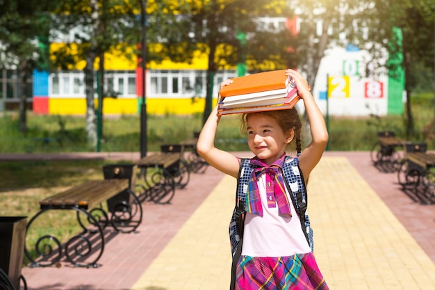 Menina com uma mochila e uma pilha de livros na cabeça perto da escola. de volta à escola