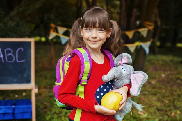 Menina com uma mochila, uma maçã e um elefante. De volta à escola. O conceito de educação, escola