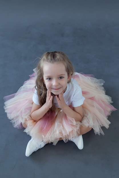 menina com uma saia se senta no chão e sorri. Roupas infantis da moda.