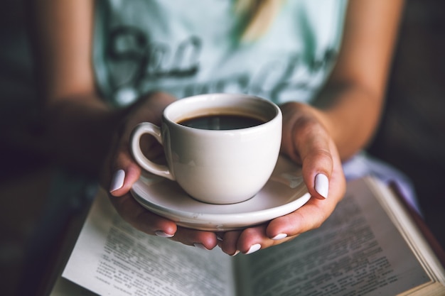 Menina com uma xícara de café e um livro. Acorda, manhã, pausa, passatempos