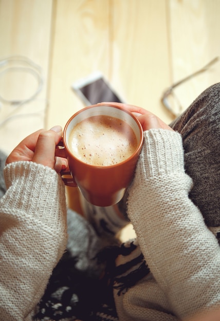 Menina com uma xícara de café sentada em um chão de madeira