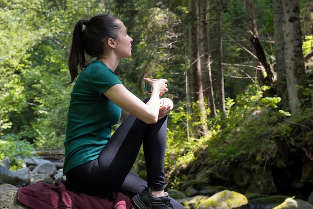 Foto menina com uma xícara de chá, sentado em uma pedra na floresta. dia de verão