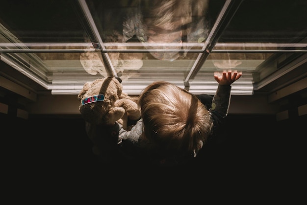 Foto menina com urso de pelúcia na janela de casa