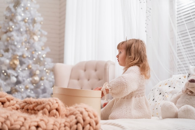 menina com vestido de malha e tiara sentada perto da árvore do White Christmas