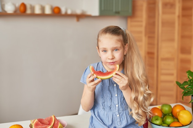 Menina come frutas na cozinha