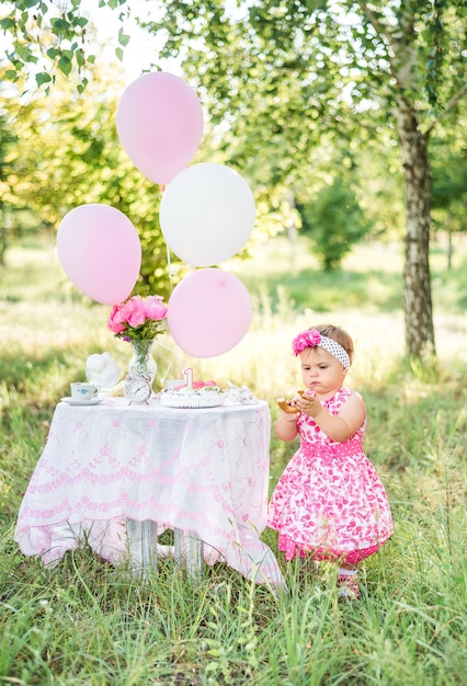 Menina comemora seu primeiro aniversário com bolo e balões na natureza