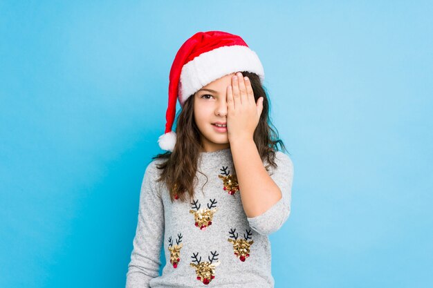 Menina comemorando o dia de Natal se divertindo cobrindo metade do rosto com palm.