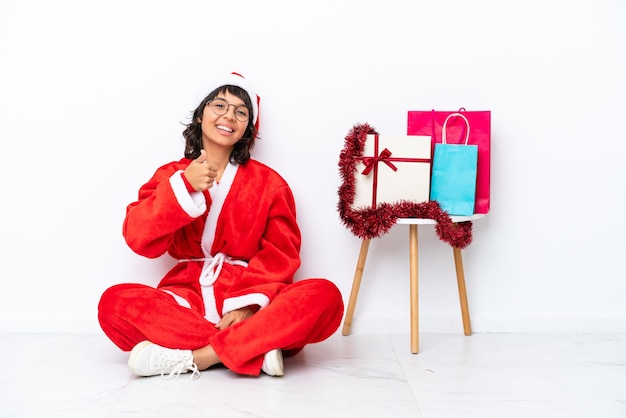 Menina comemorando o Natal sentada no chão, isolada em um fundo branco com o polegar para cima, porque algo de bom aconteceu