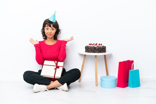 Menina comemorando seu aniversário sentada no chão, isolada no fundo branco, com expressão facial chocada