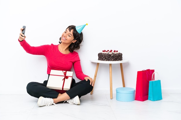 Menina comemorando seu aniversário sentada no chão, isolada no fundo branco, fazendo uma selfie