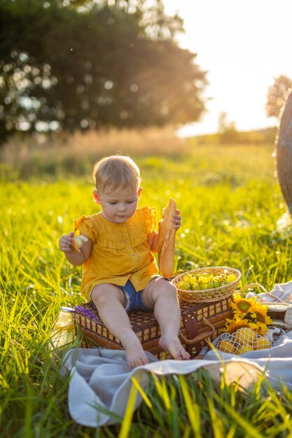 Menina comendo baguete fresca e frutas em um piquenique nas luzes do pôr do sol na natureza