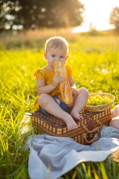 Menina comendo baguete fresca e frutas em um piquenique nas luzes do pôr do sol na natureza