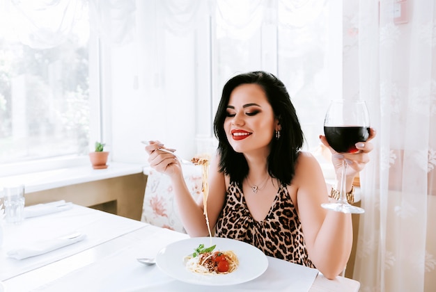 Menina comendo macarrão em um restaurante, bebendo seu vinho tinto