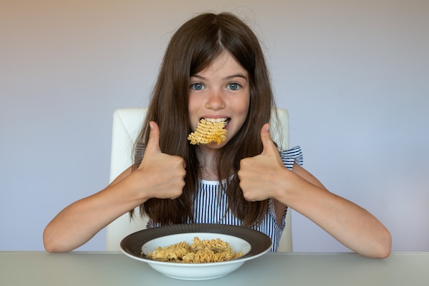 Foto menina comendo macarrão instantâneo chinês, conceito de alimentação pouco saudável, vício em comida