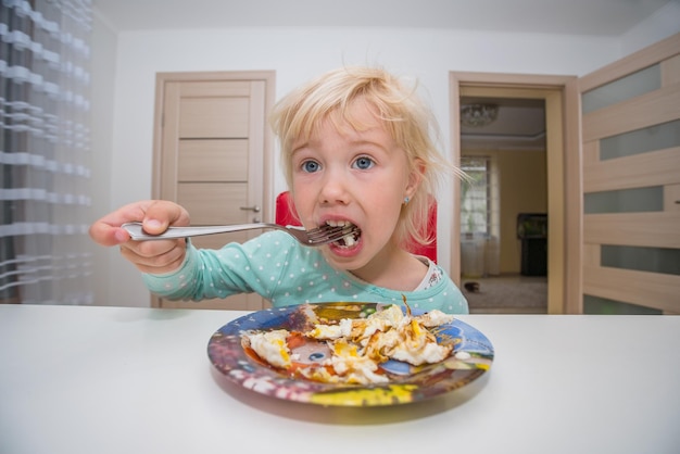 menina comendo ovos mexidos na cozinha.