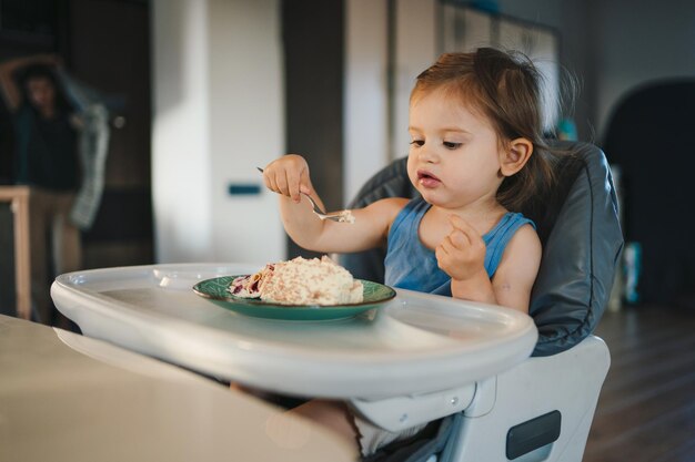 Menina comendo seu jantar enquanto está sentada em uma cadeira alta Pessoa positiva Conceito natural de comida para bebê