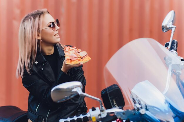 Menina comendo uma deliciosa pizza sentada em uma motocicleta