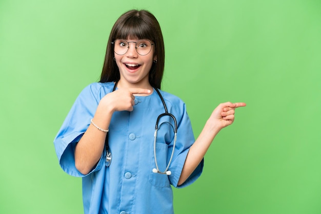 Menina como uma médica cirurgiã sobre fundo croma isolado surpreso e apontando para o lado