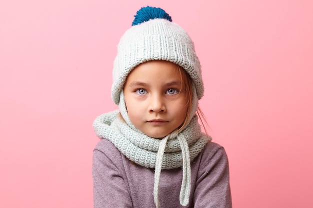 menina congelada com olhos grandes, vestindo roupas de inverno de malha sobre fundo rosa isolado