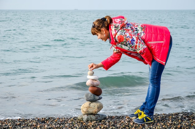 Menina constrói uma pirâmide de pedras coloridas no mar negro em batumi, geórgia.