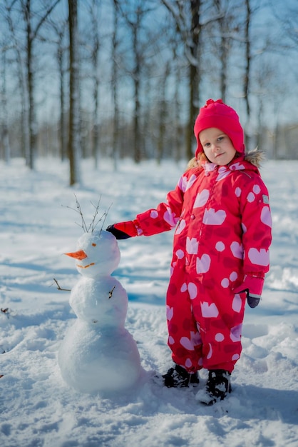 Menina construindo boneco de neve no parque nevado Lazer ativo ao ar livre com família com crianças no inverno Criança durante passeio em um parque nevado de inverno