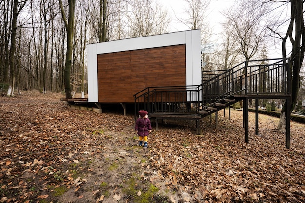 Menina contra a casa modular de um andar na floresta chuvosa de primavera