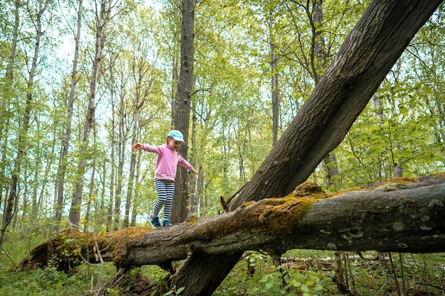 Menina corajosa na floresta de primavera andando em um log