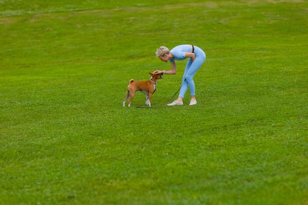 Menina corre com um cachorro no parque, no gramado ao pôr do sol, passa um animal de estimação na natureza.