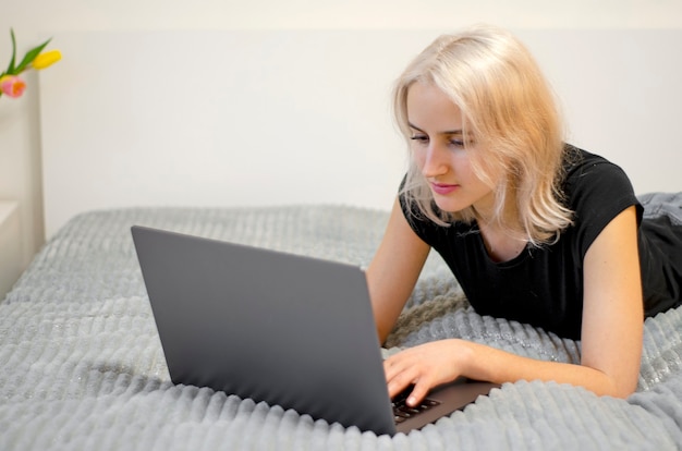 Menina corre enquanto está deitado na cama em casa. Trabalho remoto em um laptop. Trabalhe pela Internet.