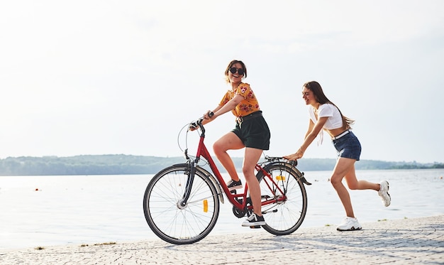 Menina corre perto de bicicleta. Duas amigas na bicicleta se divertem na praia perto do lago.