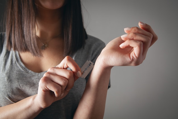 Menina corta veias com uma navalha em um cinza