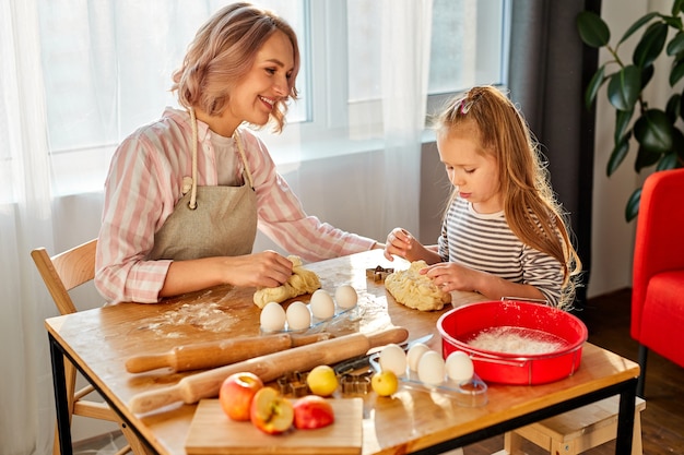 Menina criança amasse com a mãe na cozinha, indo assar biscoitos deliciosos. família em casa no fim de semana, mãe ensina a menina a cozinhar