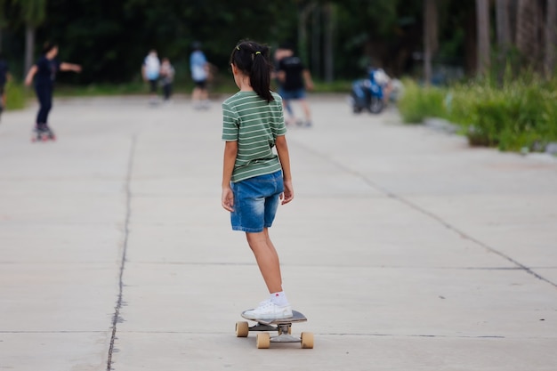 Menina criança asiática aprendendo a andar de skate ao ar livre. Criança se divertindo e jogando skate na estrada na hora do dia. Atividade infantil e o conceito de esporte radical.