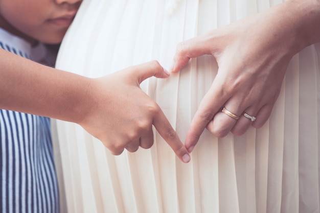 Menina criança asiática com mãe grávida fazendo com que o coração forme a forma junto na barriga da mãe, família adorável